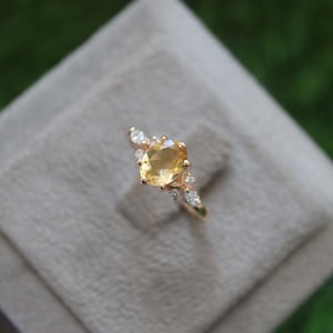 Peut inclure: Une bague en or avec une pierre ovale jaune entourée de petites pierres claires.