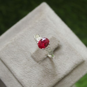 May include: A silver ring featuring a red oval gemstone surrounded by smaller white gemstones.