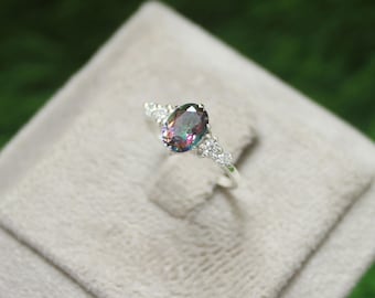 Puede incluir: Un anillo de plata con una gran piedra preciosa ovalada iridiscente rodeada de pequeñas piedras preciosas transparentes.