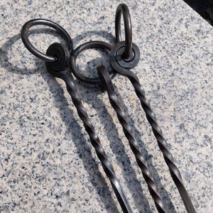 Può includere: Tre attrezzi per camino in metallo nero con manici intrecciati e estremità a forma di anello. Gli attrezzi sono disposti su una superficie di granito grigio.