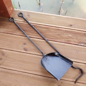 May include: A black metal fireplace shovel and poker set. The shovel has a square scoop and a curved handle. The poker has a twisted shaft and a looped handle. The set is designed for use with a fireplace or fire pit.