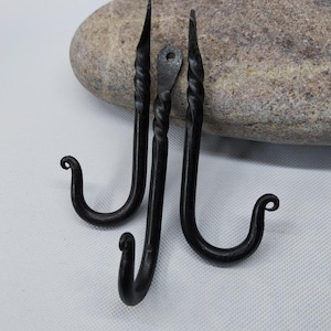 Könnte beinhalten: Drei schwarze Metallhaken mit einem gedrehten Design. Die Haken sind aus Schmiedeeisen und haben einen rustikalen Look.