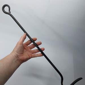 Puede incluir: Una herramienta de chimenea de metal negro con un gancho en un extremo y un gancho curvo en el otro extremo.