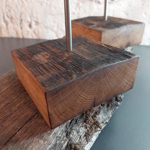 Puede incluir: Dos bloques cuadrados de madera con un acabado oscuro y texturizado. Cada bloque tiene una varilla de metal plateado que se extiende hacia arriba. Los bloques descansan sobre un trozo de madera envejecida con musgo.