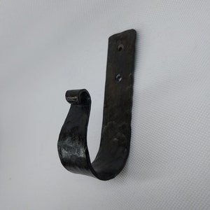 May include: Black metal hook with a curved design. The hook is mounted on a flat metal plate with three holes for attaching to a wall.