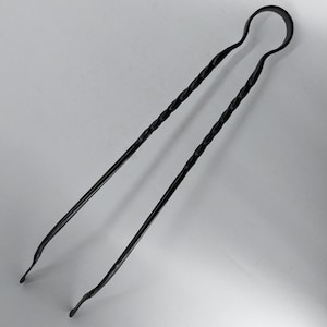 Könnte beinhalten: Schwarze Metallzange mit einem gedrehten Design. Die Zange hat einen abgerundeten Griff und ist etwa 30 cm lang.