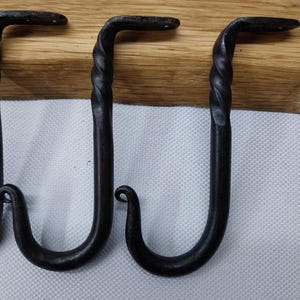 May include: Three black metal hooks with a twisted design. The hooks are mounted on a wooden surface.