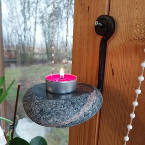 May include: A candle holder made from a natural stone with a pink candle inside. The holder is hanging from a chain attached to a metal hook.