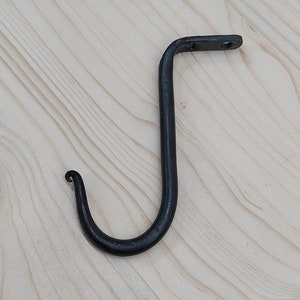 Könnte beinhalten: Ein schwarzer Haken aus Metall mit einem gebogenen Ende. Der Haken ist an einer Holzoberfläche befestigt.