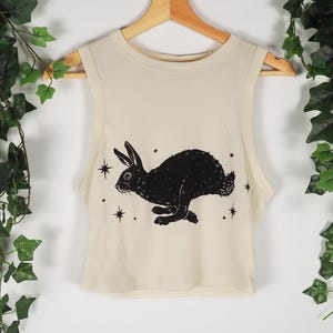 Peut inclure: Un haut court blanc sans manches avec une silhouette de lapin noir et des étoiles imprimées sur le devant.