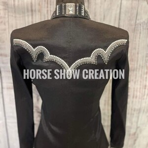 May include: Black show shirt with a white and silver trim and rhinestones. The shirt has a collar with a silver buckle and the text "HORSE SHOW CREATION" is printed on the back.