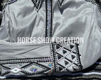 May include: A silver long-sleeved shirt with black and silver trim and rhinestones. The shirt has a geometric pattern on the cuffs and collar. The text "HORSE SHOW CREATION" is printed on the shirt.