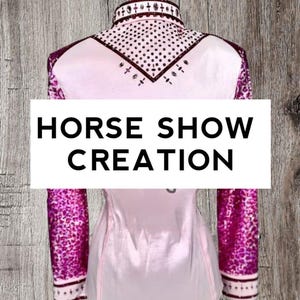 May include: Pink horse show shirt with a maroon collar and sleeves. The sleeves have a pink and maroon patterned design. The collar has rhinestones and a maroon trim. The shirt says "HORSE SHOW CREATION" on the front.