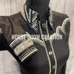 May include: Black long-sleeve shirt with a white and silver rhinestone design on the collar, cuffs, and front. The shirt has a button-up closure and a pointed collar.