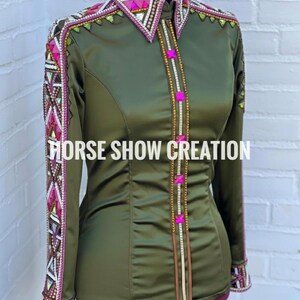 May include: Olive green long-sleeve shirt with decorative embellishments. The shirt features a pointed collar and cuffs with intricate beading and geometric patterns in pink, white, and gold. The text "HORSE SHOW CREATION" is displayed across the front.