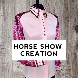 May include: A pink long-sleeved shirt with a white collar and button-up front. The sleeves are decorated with a pink and purple floral pattern. The shirt has the text "HORSE SHOW CREATION" printed on the front.