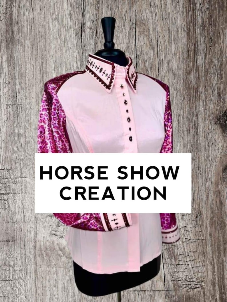 May include: A pink long-sleeved shirt with a white collar and button-up front. The sleeves are decorated with a pink and purple floral pattern. The shirt has the text "HORSE SHOW CREATION" printed on the front.