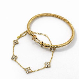 May include: A gold-toned bracelet and a delicate chain bracelet with clover-shaped accents. The bangle has a textured design, while the chain bracelet features sparkling stones. Both pieces are displayed on a white background.