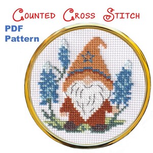 May include: A counted cross stitch PDF pattern featuring a gnome with a brown hat and beard, blue flowers, and a gold hoop frame. The text "Counted Cross Stitch" and "PDF Pattern" are displayed.