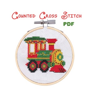 May include: Counted cross stitch PDF pattern of a red, green, and yellow toy train with lights on the front. The train is in a wooden embroidery hoop.