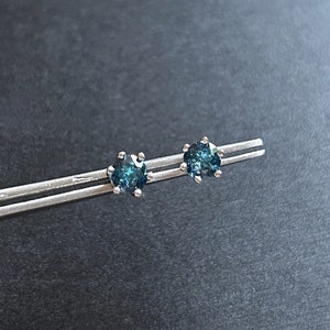 May include: A pair of silver stud earrings with small, round, dark blue gemstones.