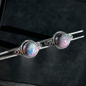 Peut inclure: Deux bagues en argent avec des pierres précieuses rondes, roses, bleues et grises. Les bagues sont présentées sur une surface noire.