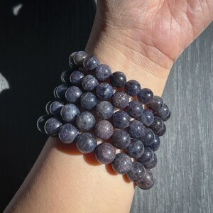 May include: A stack of dark blue beaded bracelets. The round beads have a speckled appearance and are strung together on an elastic band. The bracelets are worn on a wrist, with the skin tone visible.