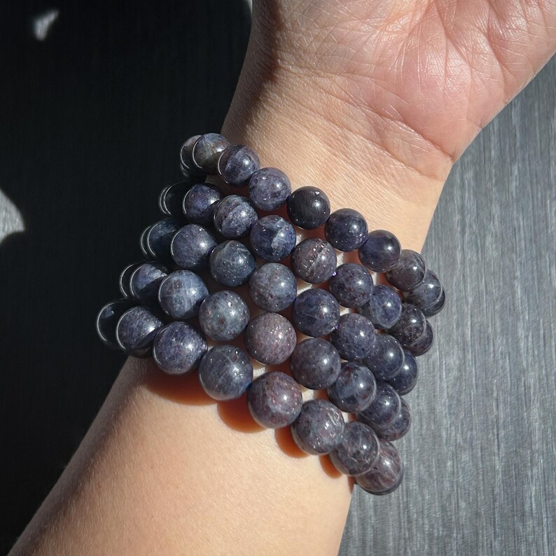 May include: A stack of dark blue beaded bracelets. The round beads have a speckled appearance and are strung together on an elastic band. The bracelets are worn on a wrist, with the skin tone visible.