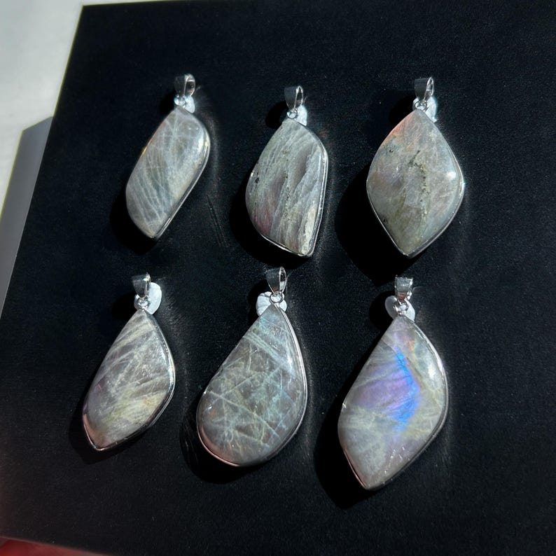Pu&ograve; includere: Sei ciondoli con pietre preziose con montature in metallo color argento. I ciondoli hanno forme diverse e mostrano una gamma di colori, tra cui grigio, viola e blu. I ciondoli sono esposti su una superficie nera.
