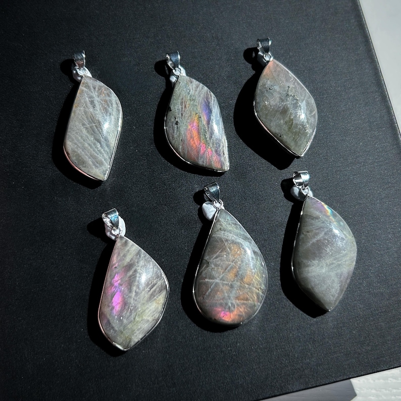 Pu&ograve; includere: Sei ciondoli in labradorite iridescente con bails color argento. I ciondoli hanno una forma a goccia o a foglia, con un mix di colori grigi, viola e blu. I ciondoli sono esposti su una superficie scura.