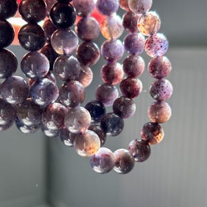 May include: Strands of gemstone beads in shades of purple, brown, and cream. The beads are round and appear to be strung together to form a bracelet or necklace. The beads have a polished, glossy finish.