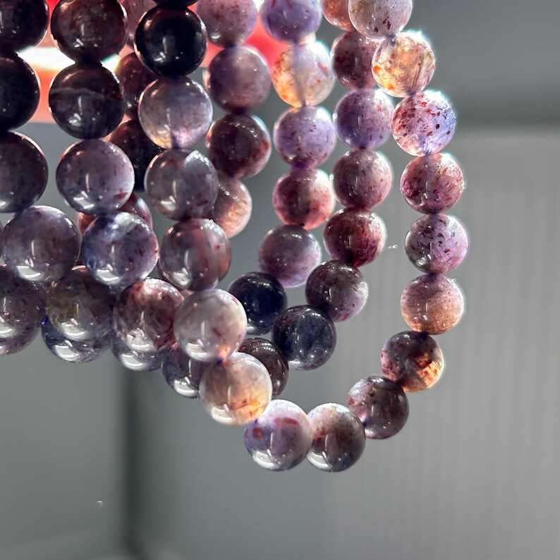 May include: Strands of gemstone beads in shades of purple, brown, and cream. The beads are round and appear to be strung together to form a bracelet or necklace. The beads have a polished, glossy finish.
