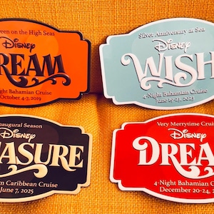 May include: Four Disney cruise name tags with the words DREAM, WISH, and TREASURE. The tags are orange, light blue, black, and red. Each tag has the Disney logo and cruise details, including dates and destinations.