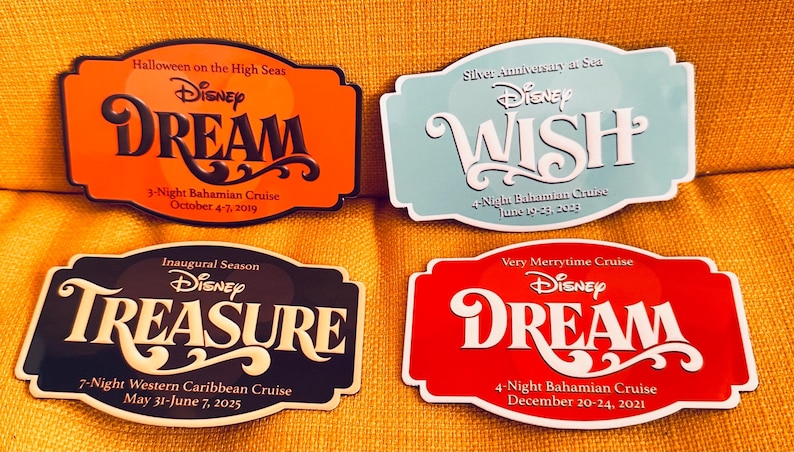 May include: Four Disney cruise name tags with the words DREAM, WISH, and TREASURE. The tags are orange, light blue, black, and red. Each tag has the Disney logo and cruise details, including dates and destinations.
