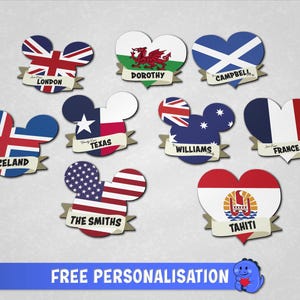 May include: A collection of heart-shaped and Mickey-ear-shaped ornaments featuring various national and regional flags. Each piece includes a banner with printed text such as London, Dorothy, Campbell, Iceland, Texas, Williams, France, The Smiths, and Tahiti.