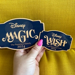 May include: Two navy blue Disney cruise signs. One says "MAGIC" with "The Patterson Family 2024". The other says "WISH" with "4 Night Bahamian Cruise 2024". Both have a cream-colored font.