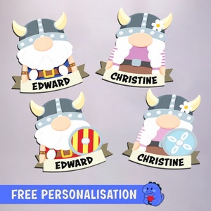 May include: Four personalized Viking gnome ornaments with names "Edward" and "Christine". Each gnome has a different colored shield and a white flower on their hat.