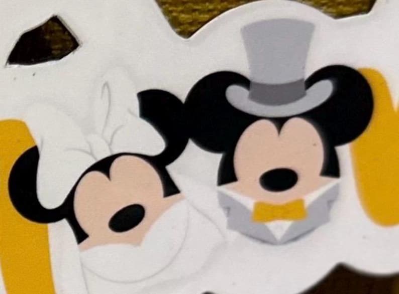 Op de afbeelding: Een gestanste sticker met de hoofden van twee tekenfilmmuizen. De linker muis draagt een grote witte strik en een witte sluier. De rechter muis draagt een grijze hoge hoed, een grijs smokingjasje en een gele vlinderdas.