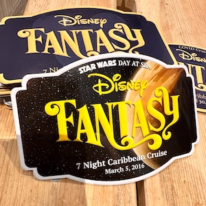 May include: Several Disney Fantasy cruise signs. The signs have a navy blue and black background with yellow text that reads "Disney FANTASY". One sign is for a "7 Night Caribbean Cruise" on March 5, 2016, with "Star Wars Day at Sea".