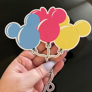 Pode incluir: Tr&ecirc;s bal&otilde;es em forma de Mickey Mouse nas cores azul, rosa e amarelo. Os bal&otilde;es est&atilde;o amarrados com um cord&atilde;o.