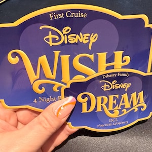 May include: Two Disney cruise ship magnets. The larger magnet reads "Disney WISH" in gold lettering on a blue background. The smaller magnet reads "Disney DREAM" in gold lettering on a blue background.