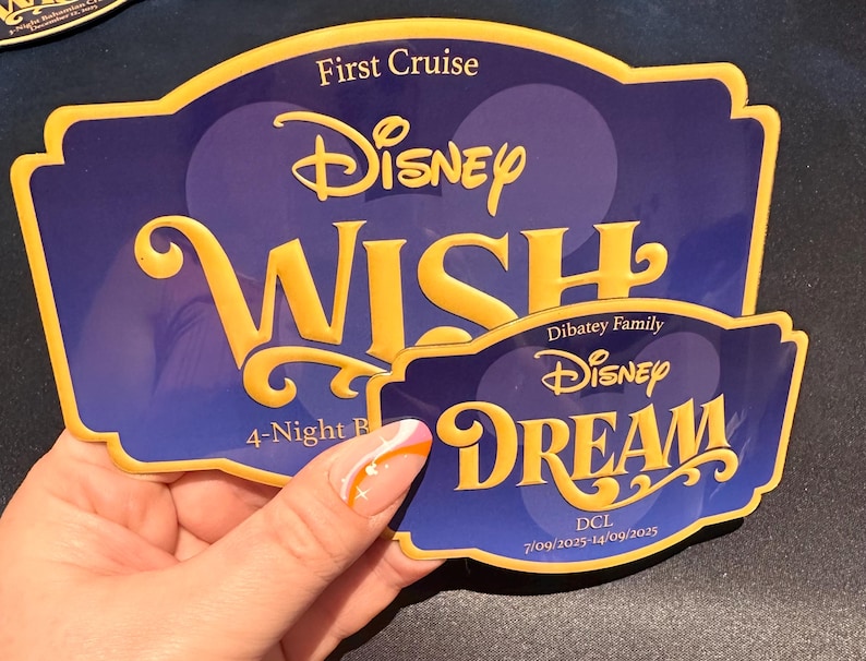 May include: Two Disney cruise ship magnets. The larger magnet reads "Disney WISH" in gold lettering on a blue background. The smaller magnet reads "Disney DREAM" in gold lettering on a blue background.