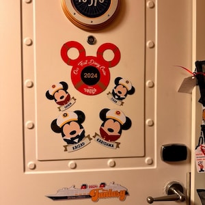 May include: A white door decorated with Disney-themed stickers. A circular sign displays the number 10576. Mickey Mouse stickers with names and a cruise ship sticker that says "Fantasy" are also visible.