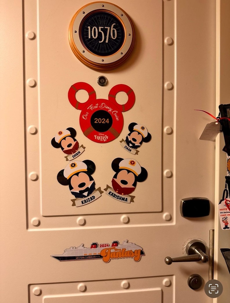 May include: A white door decorated with Disney-themed stickers. A circular sign displays the number 10576. Mickey Mouse stickers with names and a cruise ship sticker that says "Fantasy" are also visible.