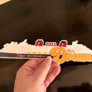 May include: A white and navy blue cruise ship sticker with the text "Disney Dream" in orange script. The sticker also includes the text "2023" and "7-Night Mediterranean". The ship has red and black Mickey Mouse ears.