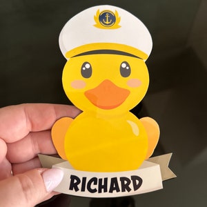 May include: A yellow rubber duck illustration wearing a white captain's hat with a blue and gold anchor emblem. The duck has an orange beak and pink cheeks. Below the duck is a white banner with the name RICHARD printed in black letters.