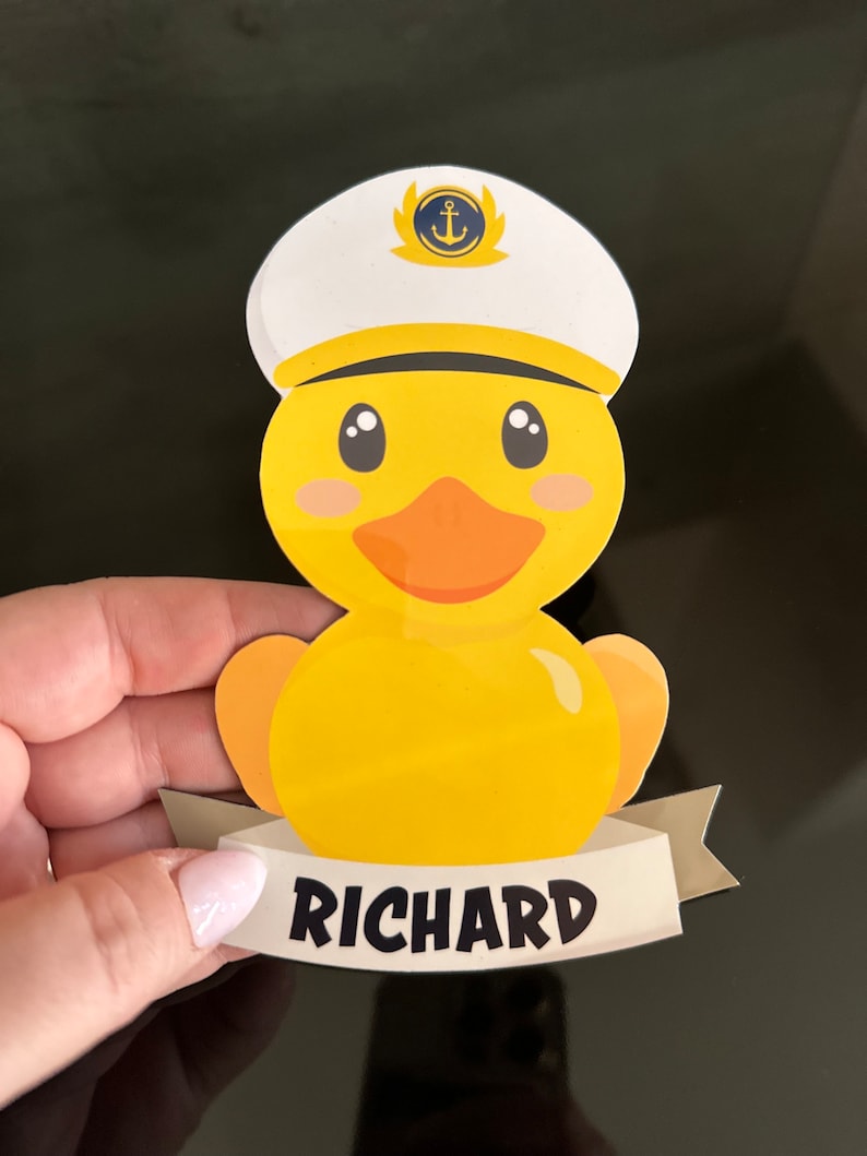 May include: A yellow rubber duck illustration wearing a white captain's hat with a blue and gold anchor emblem. The duck has an orange beak and pink cheeks. Below the duck is a white banner with the name RICHARD printed in black letters.