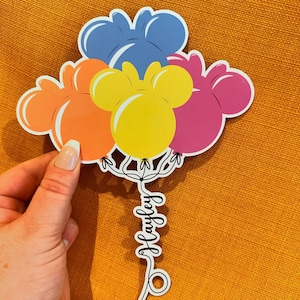Pode incluir: Um conjunto de cinco bal&otilde;es de papel coloridos com orelhas de Mickey Mouse. Os bal&otilde;es s&atilde;o azuis, laranja, amarelos, rosa e roxos. Os bal&otilde;es est&atilde;o amarrados com um cord&atilde;o que diz "Hawley".