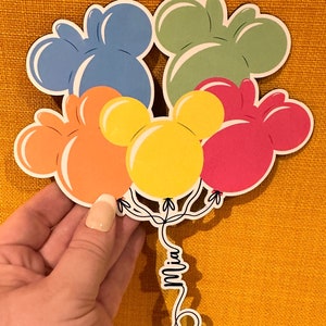 Pode incluir: Um conjunto de seis bal&otilde;es coloridos em forma de Mickey Mouse com o nome "Mia" escrito na corda.