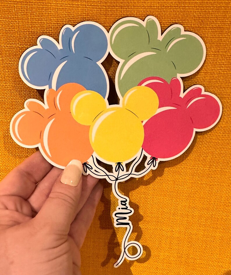 Pode incluir: Um conjunto de seis bal&otilde;es coloridos em forma de Mickey Mouse com o nome "Mia" escrito na corda.